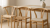 Editorial Scandinavian dining scene showing three Y-chair style options with different wood finishes and seat material textures (woven and upholstered), captured in realistic daylight.