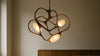 A sculptural statement pendant chandelier glows above a living room seating area, balanced with natural textures and realistic warm lighting.
