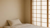 Hero shot of a calm, compact Japanese bedroom with an affordable-looking bed and layered bedding under soft shoji light.